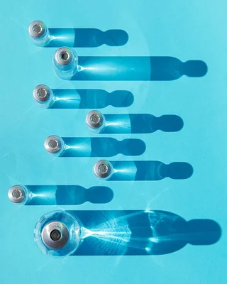 Flacons de peptides anti-âge présentés sur fond bleu clair, leurs ombres évoquant des silhouettes.