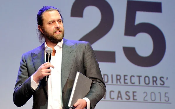 Carl Rinsch en costume gris parlant dans un micro lors du '25 DIRECTORS' SHOWCASE 2015'