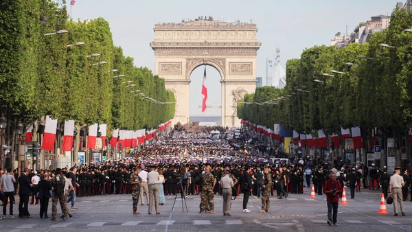 Foule nombreuse et défilé militaire sur les Champs-Élysées le 14 juillet, avec l'Arc de Triomphe en arrière-plan