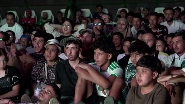 Supporters algériens déçus assistant à un match dans un stade, après l'élimination des Fennecs de la Coupe du Monde.
