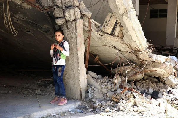 Une enfant au milieu des ruines d'un bâtiment effondré en Syrie, symbole des ravages de la guerre.