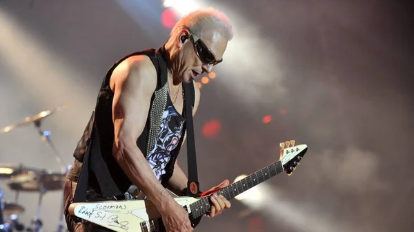 Musicien chauve aux lunettes de soleil jouant de la guitare électrique blanche sur la scène du Hellfest.