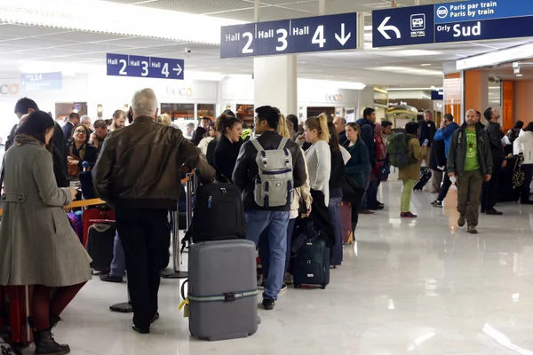 Voyageurs en file d'attente dans le terminal d'Orly, près des panneaux de direction.