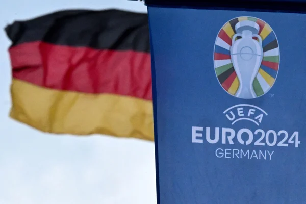 Bannière officielle de l'EURO 2024 avec le logo du tournoi, devant un drapeau allemand en arrière-plan.