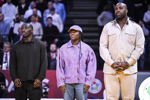 Cérémonie d'avant-match sur un terrain de basket, avec des judokas et officiels.