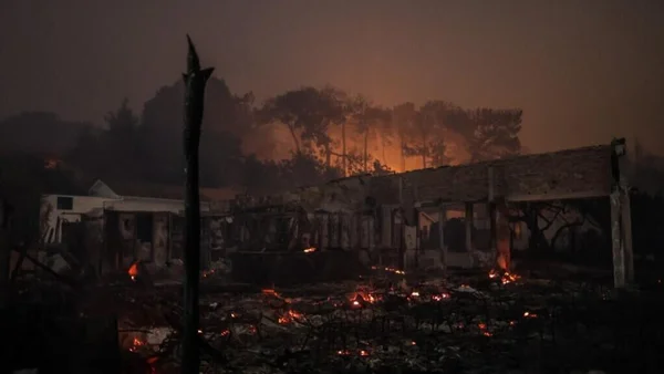 Les ruines calcinées d'un bâtiment après le passage d'un incendie de forêt, avec des braises encore ardentes.