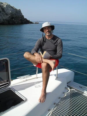 Julien Poublan lisant sur le pont de son catamaran, entouré de l'océan et des falaises.