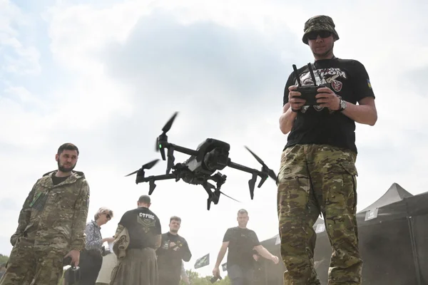 Opérateur de drone en tenue militaire manipulant un engin en extérieur, entouré d'autres militaires.