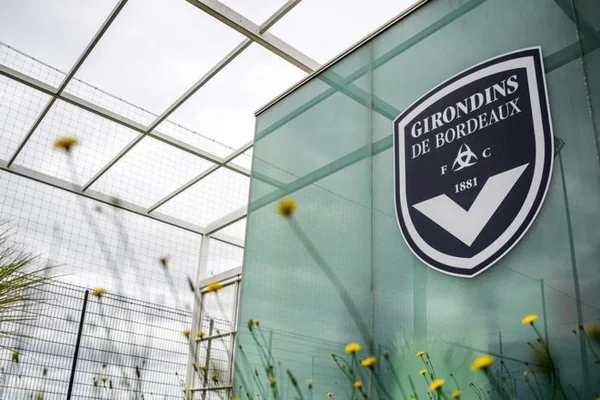Le blason des Girondins de Bordeaux sur un mur en verre, entouré de fleurs sauvages.