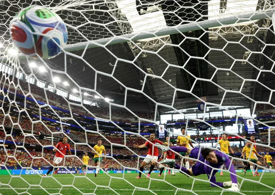 Un ballon de football heurte le fond du filet alors que le gardien plonge en vain lors d'un match en stade.