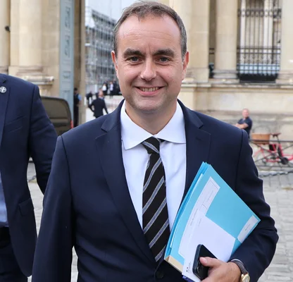 Sébastien Lecornu souriant devant un bâtiment officiel avec des dossiers.