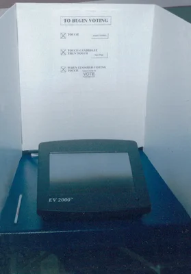 Machine à voter électronique EV 2000 dans un isoloir, avec des instructions de vote affichées.