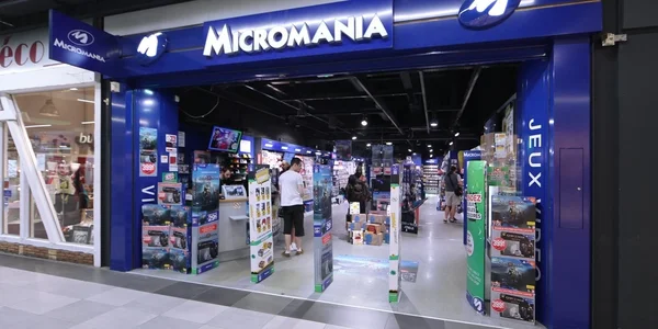 Entrée d'un Micromania en centre commercial, avec clients et présentoirs.