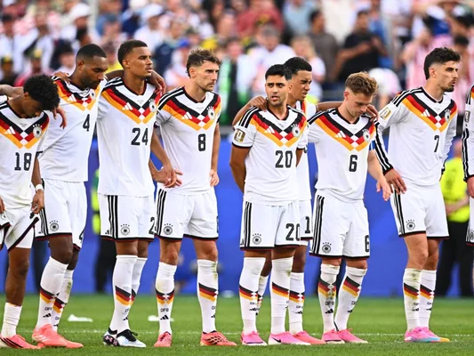 Les joueurs de l'équipe d'Allemagne alignés sur la pelouse avant un match, dans une atmosphère solennelle.
