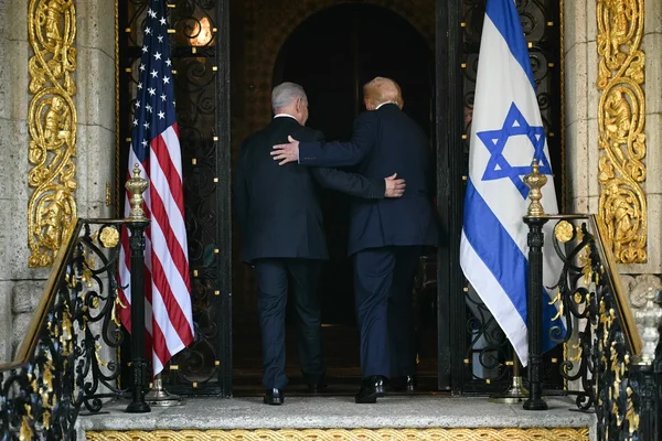 Benjamin Netanyahu et un responsable américain entrant dans un bâtiment officiel, encadrés par les drapeaux des deux nations.