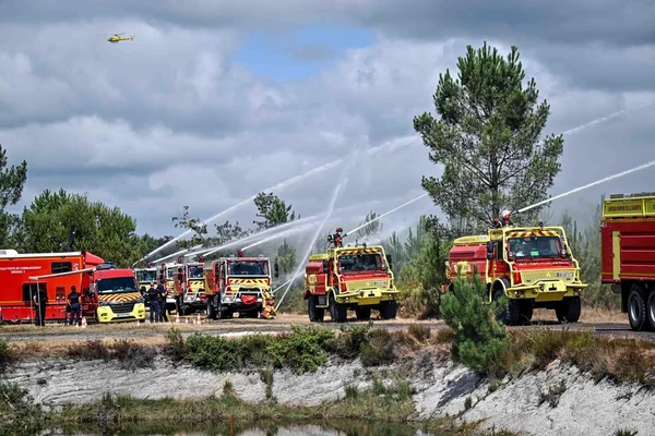 Des camions de pompiers en action lors d'un incendie, avec un hélicoptère en soutien.