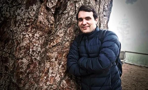 Christophe Gleizes appuyé contre un arbre, en veste bleue.