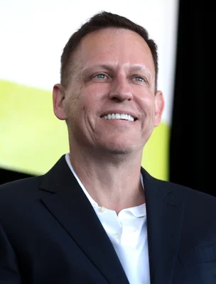 Peter Thiel en costume sombre, souriant devant un fond flou.