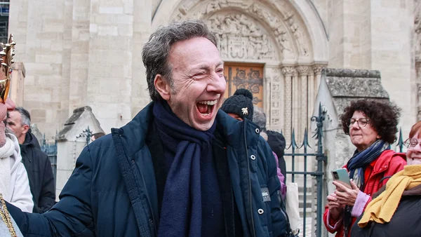 Stéphane Bern, souriant, entouré de passants devant un édifice en pierre à Saint-Denis.