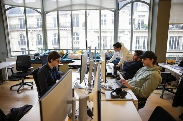 Employés de Hugging Face dans leur bureau parisien, un open space lumineux avec vue sur des immeubles haussmanniens.