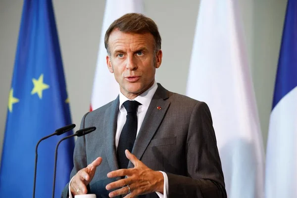 Emmanuel Macron s'exprime lors d'une conférence de presse, entouré des drapeaux de l'Union européenne et de la France.