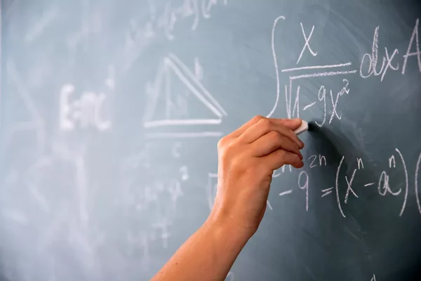 Main écrivant une équation mathématique sur un tableau vert, illustrant le travail des mathématiciens.