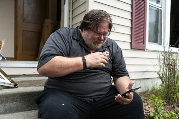Suspect recherché dans les fusillades politiques du Minnesota, assis sur des marches en regardant son téléphone.
