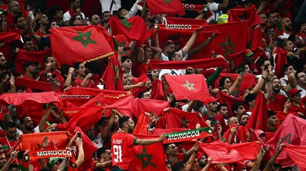 Supporters marocains dans un stade, brandissant des drapeaux et des écharpes aux couleurs du Maroc.