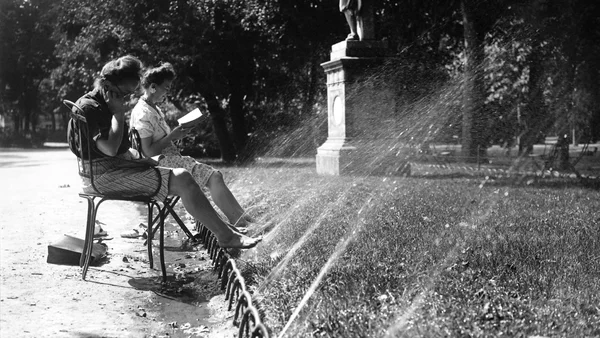 Deux femmes se rafraîchissent sous un arroseur dans un parc lors d'une canicule passée.