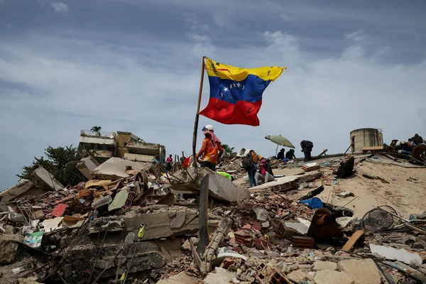 Le drapeau du Venezuela flotte sur les ruines après les séismes, tandis que les secouristes s'affairent.