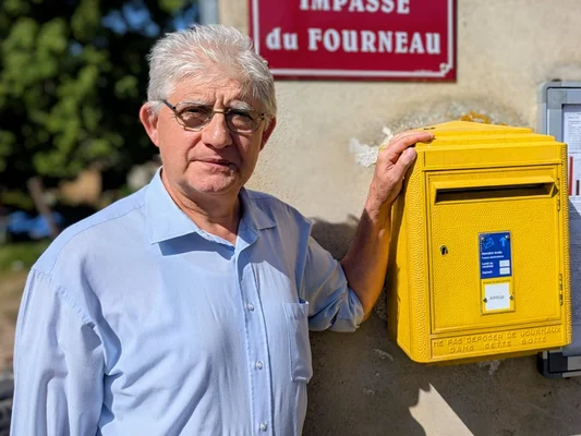 Un habitant devant une boîte aux lettres jaune à Côte-d'Or, symbole du service postal en déclin.