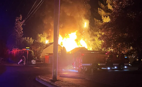 Incendie nocturne d'une structure résidentielle avec un camion de pompiers au premier plan.