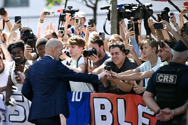 Zinédine Zidane salue les supporters derrière les barrières de sécurité, sous l'œil des CRS.