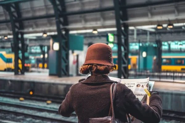 Un voyageur sur un quai de gare, observant les trains, illustrant l'ambiance des départs en train de nuit.