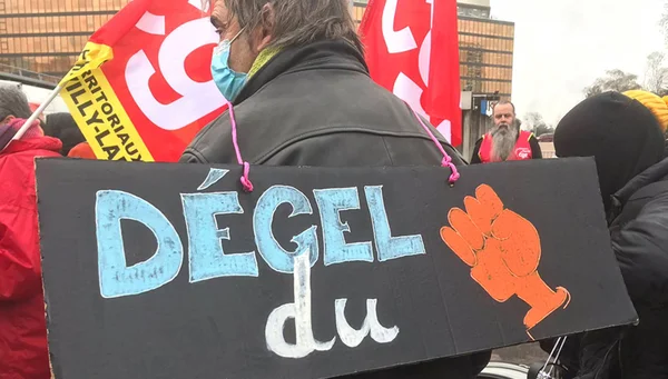 Appel à la grève du 29 septembre : un manifestant avec une pancarte ‘Dégel du’ et des drapeaux rouges.