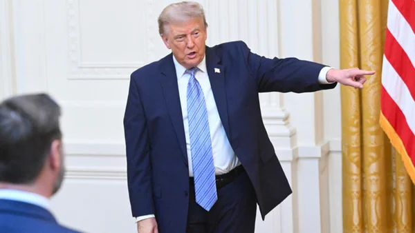 Donald Trump pointant du doigt à l'intérieur, avec un drapeau américain en arrière-plan.