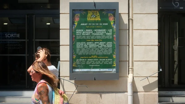 Affiche du Delta Festival sur un mur en pierre, avec des passants dans une rue de Marseille.
