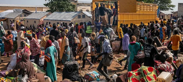 Des personnes déplacées rassemblées avec leurs bagages près d'un camion jaune dans une zone poussiéreuse du Soudan du Sud.