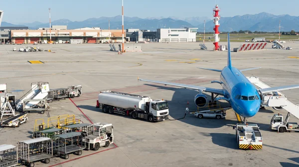 Un avion KLM en cours de ravitaillement en carburant sur un tarmac d'aéroport avec des montagnes en arrière-plan.