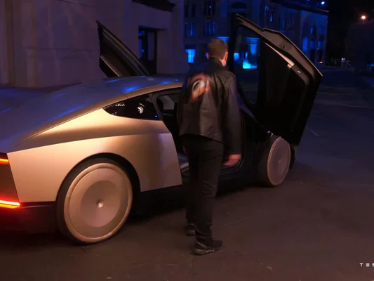 Un homme monte dans un Cybercab argenté aux portes relevables, de nuit.