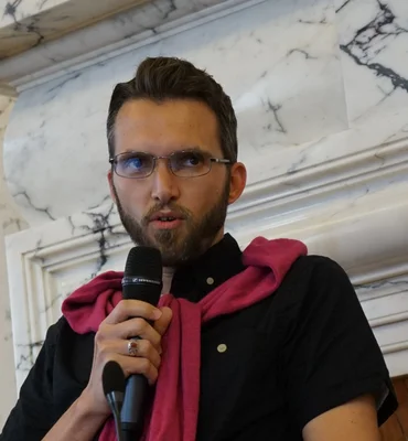 Ludovic-Mohamed Zahed s'exprimant au micro devant une cheminée en marbre.