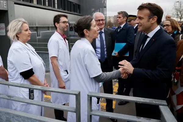 Emmanuel Macron en visite dans un établissement de santé, serrant la main d'une soignante.