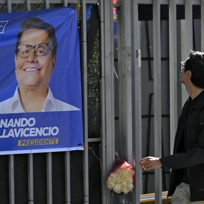 Mémorial improvisé avec un bouquet de roses blanches devant un panneau de campagne de Fernando Villavicencio.
