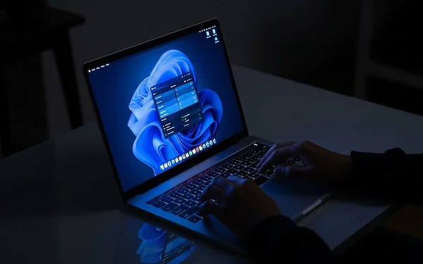 Personne tapant sur un ordinateur portable dans une pièce sombre, illustrant l'utilisation d'un PC sous Windows.
