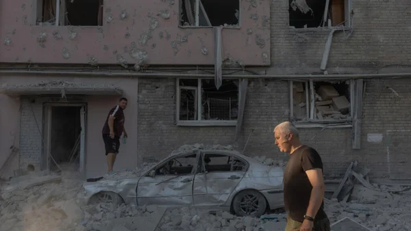 Deux hommes dans une rue dévastée de Kiev, avec une voiture endommagée et des immeubles touchés par les frappes.