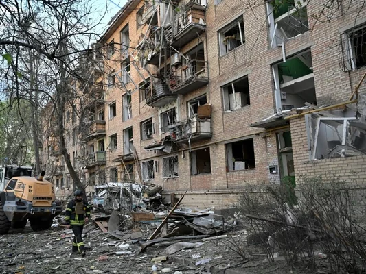 Un immeuble d'habitation lourdement endommagé à Kiev, avec un pompier et un engin de chantier dans les décombres.