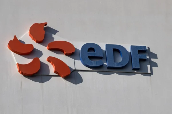 Logo tridimensionnel d'EDF sur fond blanc, éclairé par le soleil.