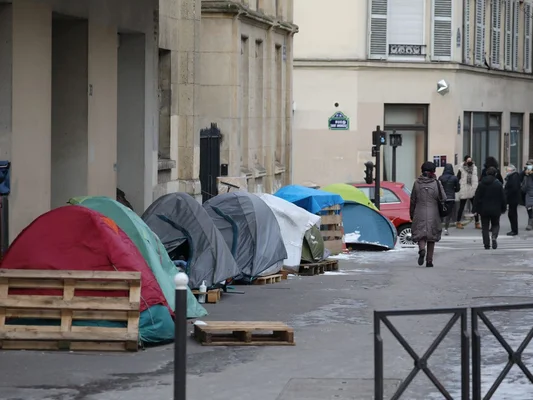 Campement de sans-abri sous des tentes le long d'une rue en ville.