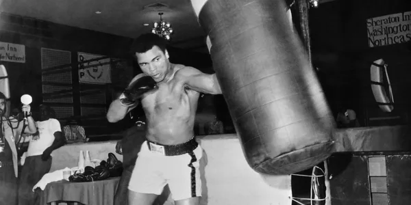 Mohamed Ali s'entraînant au sac de frappe dans une salle de boxe, image emblématique de sa préparation physique.