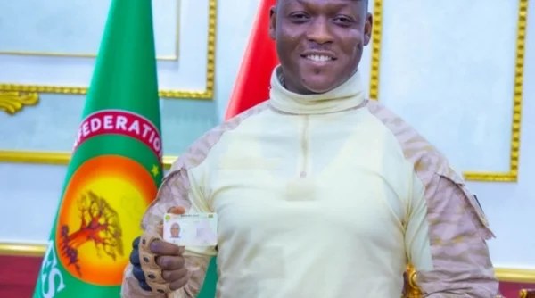 Le président Ibrahim Traoré arborant une carte d'identification devant le drapeau de la Fédération des États du Sahel.